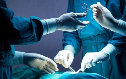 doctor and nurse medical team are performing surgical operation at emergency room in hospital. assistant hands out scissor and instruments to surgeons during operation.